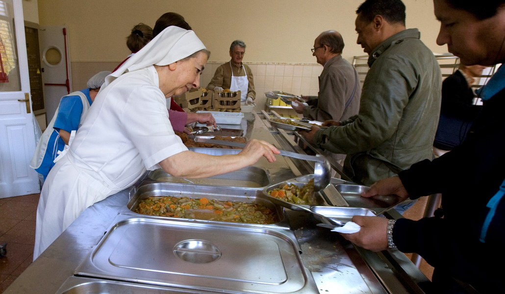 Una religiosa sirve comida a los usuarios de un comedor social apoyado por Aaqua